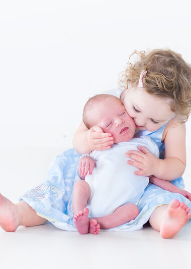 Sweet toddler girl kissing her newborn baby brother