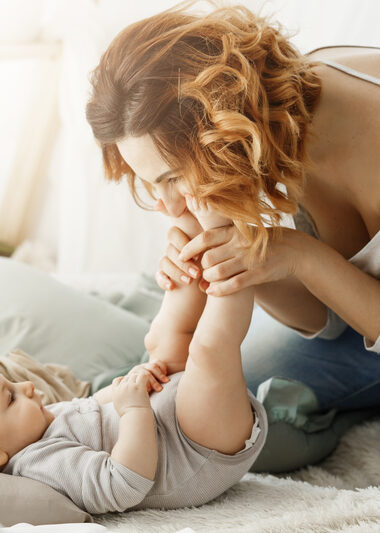 Happy mother playing with newborn baby spending best maternity moments in cozy bedroom. Warm family atmosphere. Family concept