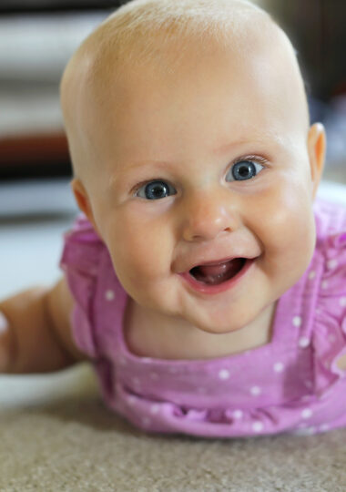 A happy 6 month old baby girl is laying on her tummy at home smiling and trying to crawl.